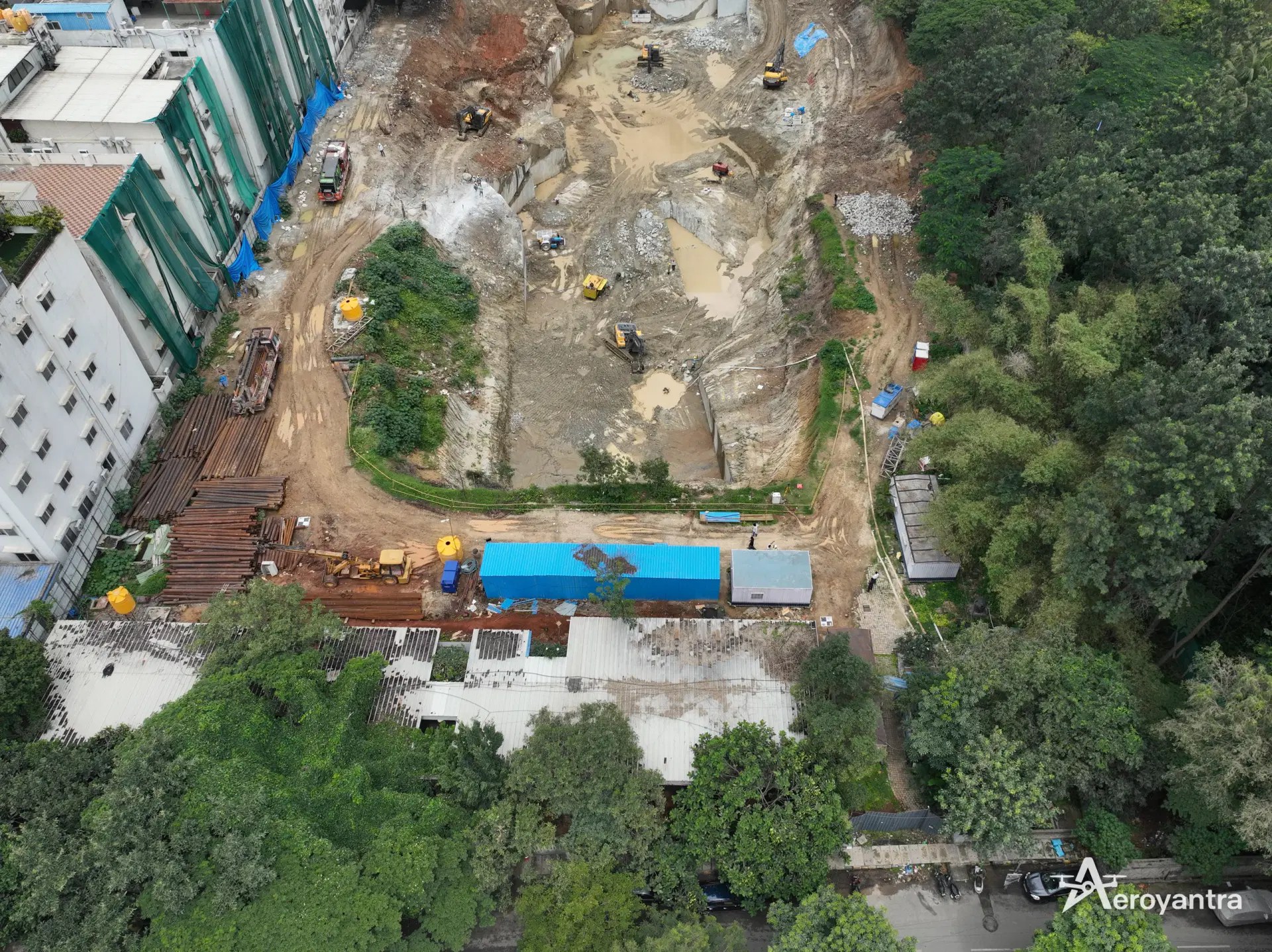 Aerial drone photograph of a deep basement excavation with excavators, site cabins and stacked steel casing